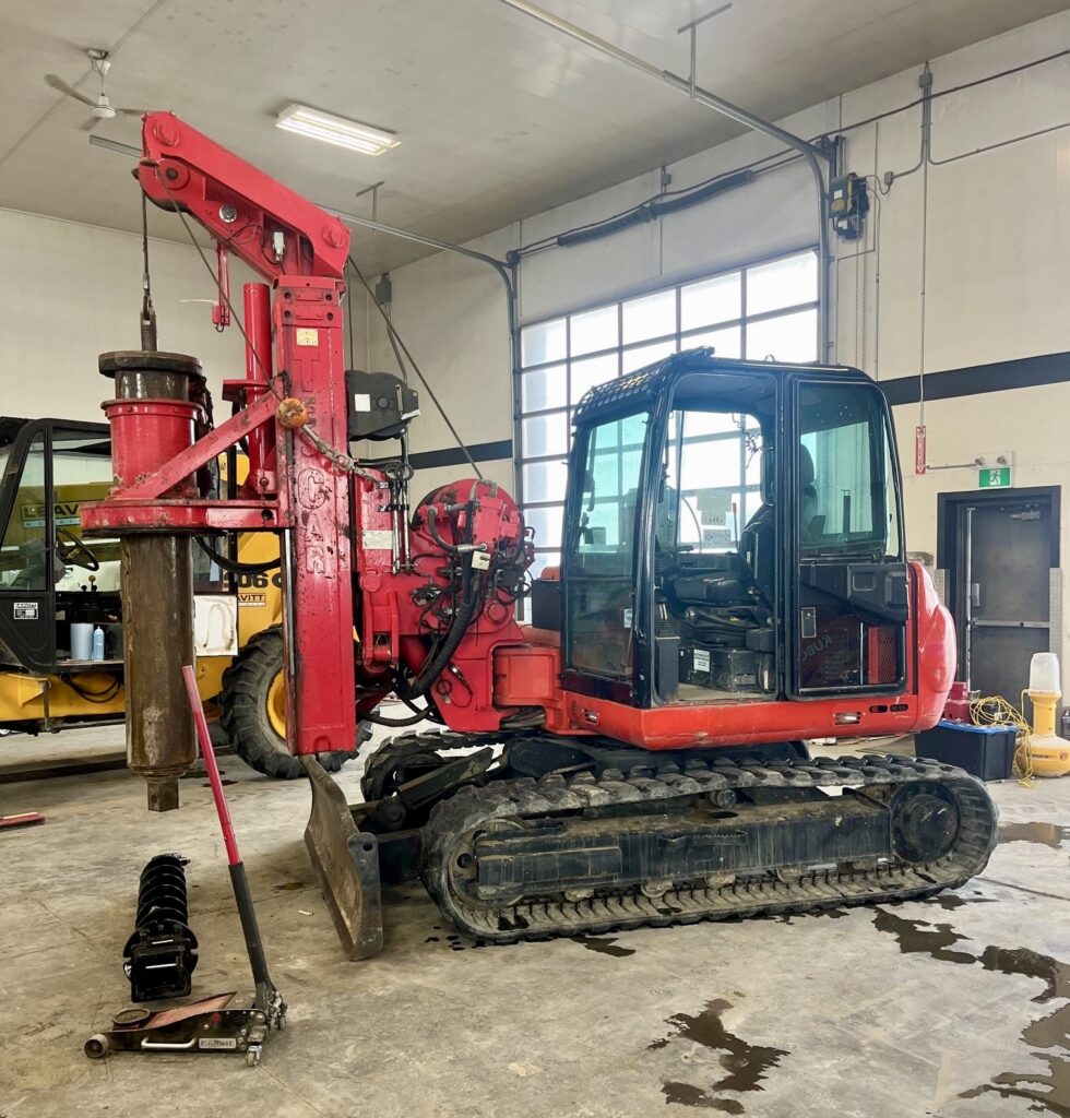 A red backhoe excavator parked alongside other machines in a garage.
