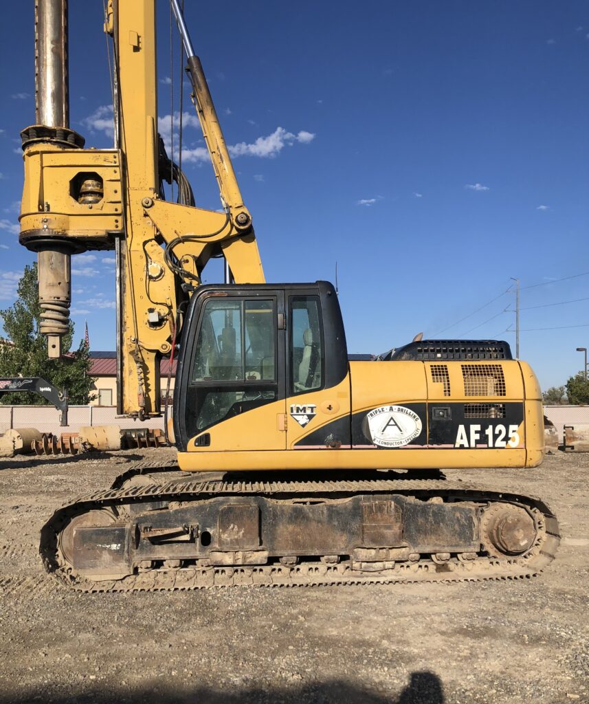 A yellow and black backhoe excavator parked on dirt.