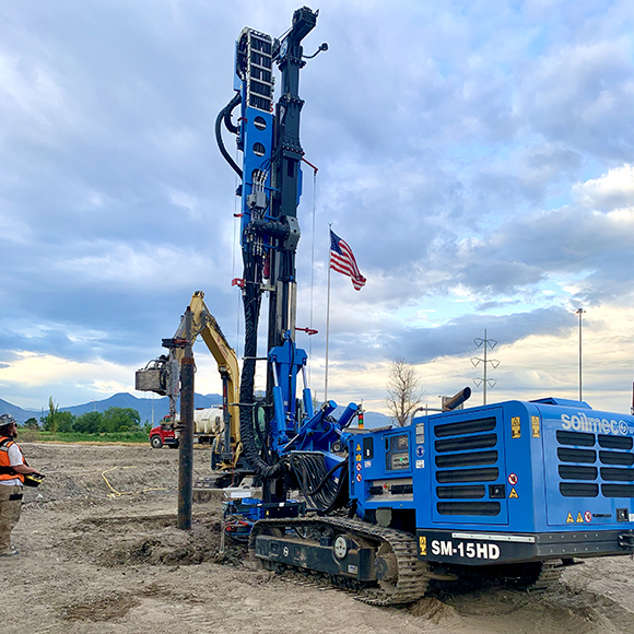 A blue drill rig sits on the ground in a field, ready for work.