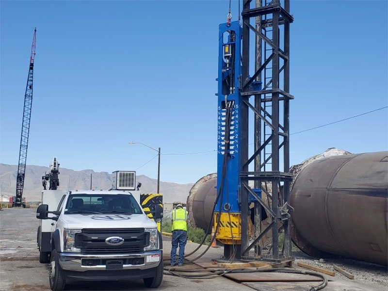 A truck parked next to a large pipe with a crane nearby.