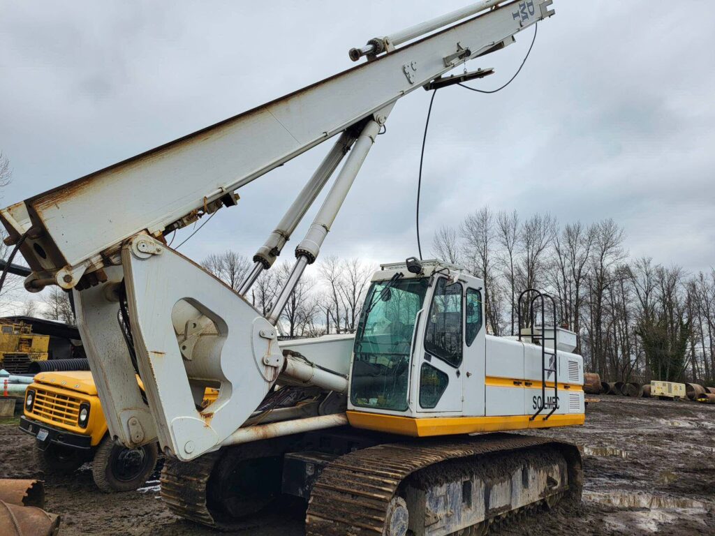 A crane perched on a muddy field, with a backhoe nearby.