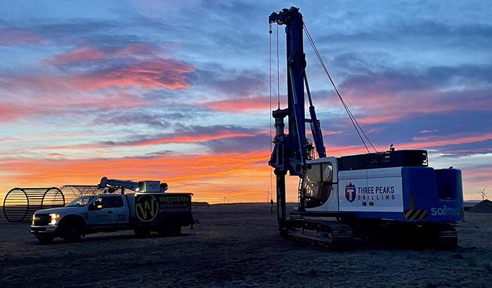 A crane and a truck in a field at sunset, showcasing equipment solutions for foundation drilling.