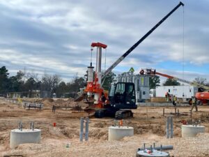 A crane lifts a large piece of equipment at a busy construction site under a clear blue sky