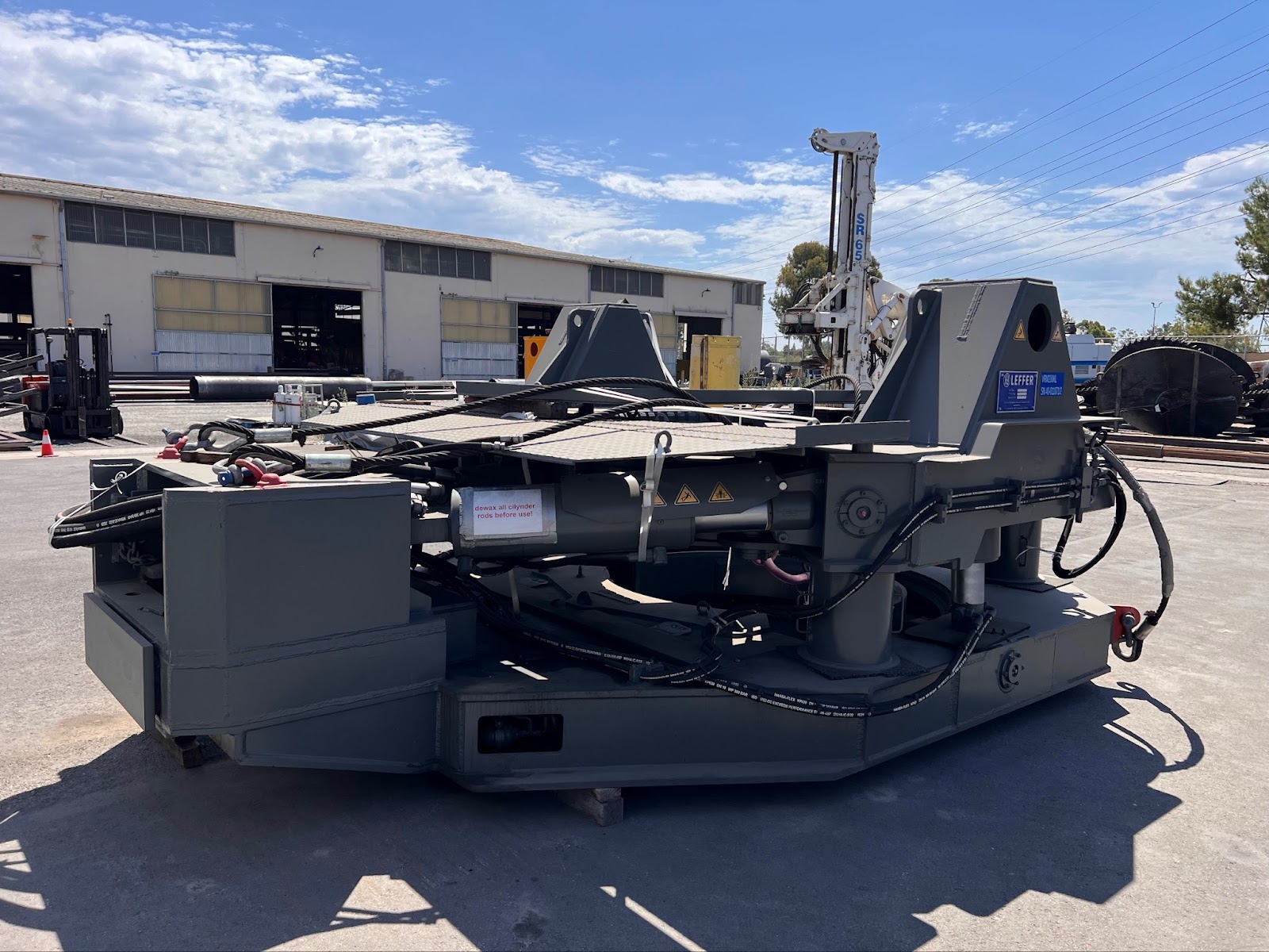 Heavy-duty construction equipment attachment placed outdoors on a concrete surface near an industrial warehouse.