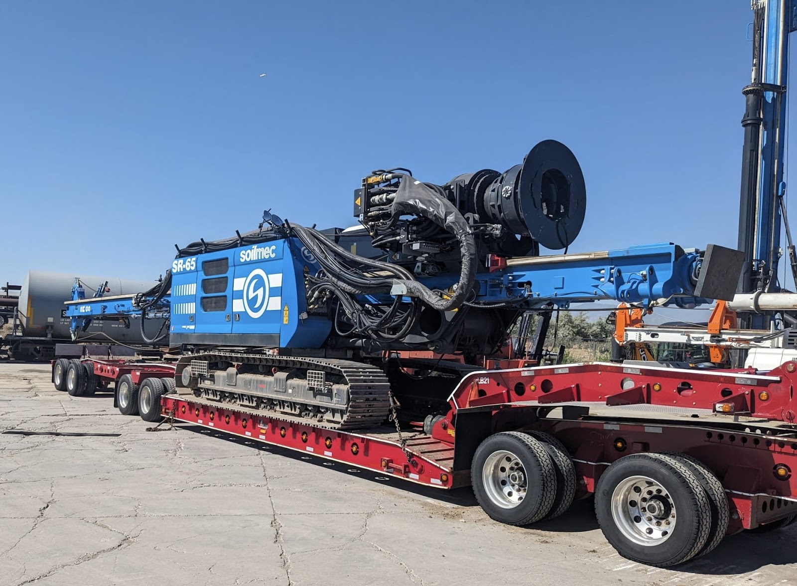 Heavy-duty Soilmec SR-65 drilling rig loaded on a red transport trailer.