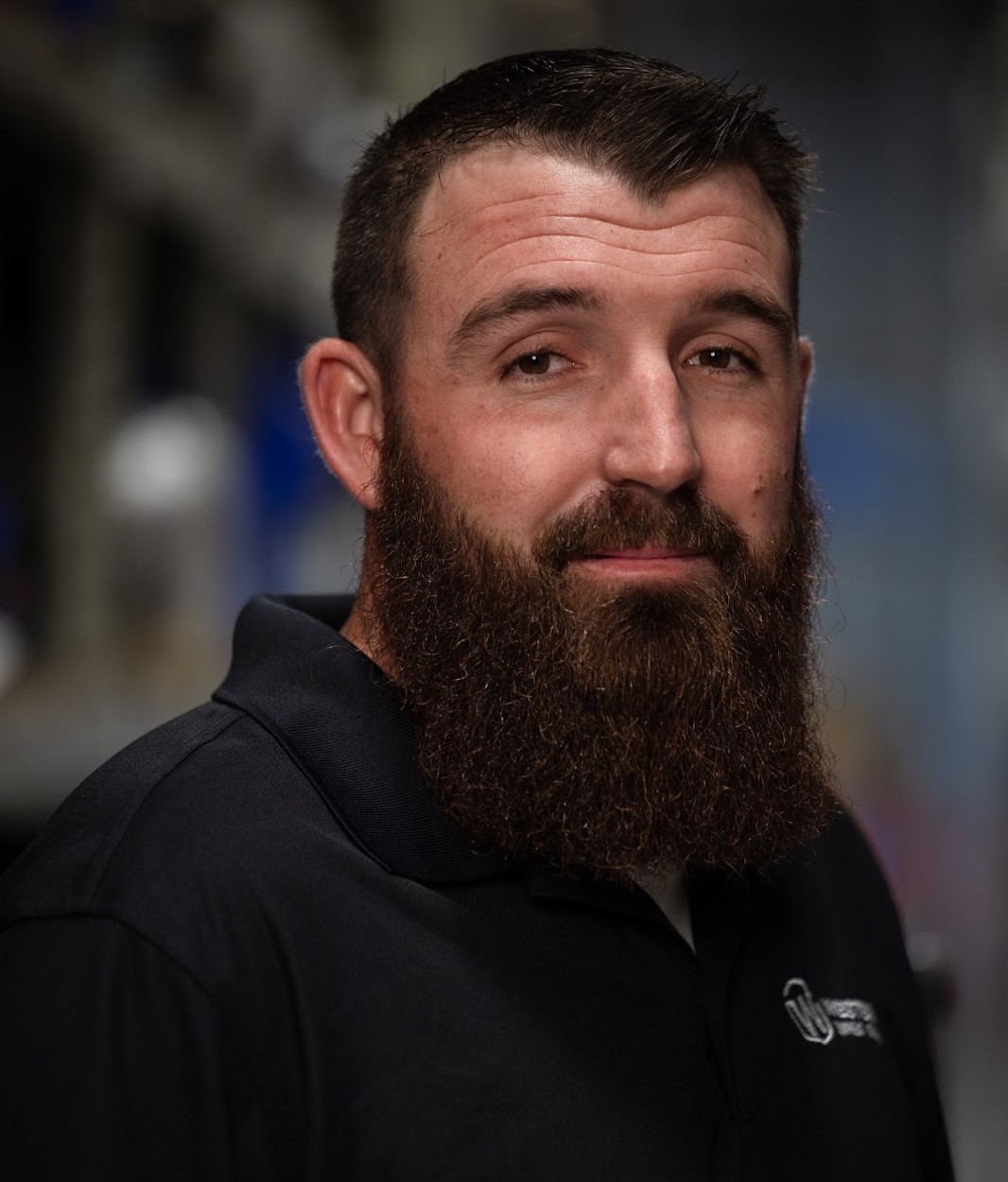 Man with a beard wearing a black polo shirt with a logo.