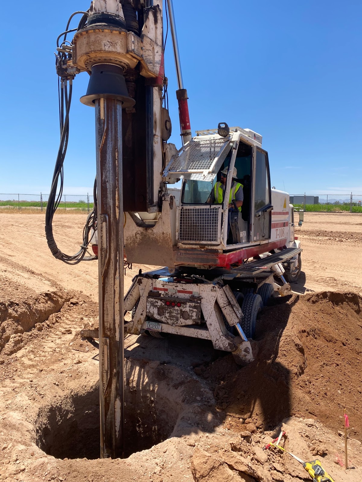 A construction worker operating a truck-mounted drilling rig to bore a hole into the earth at a construction site.