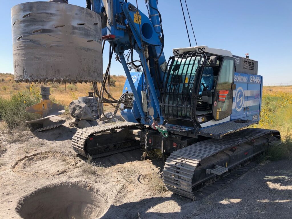 Blue excavator drilling into large rock for foundation work